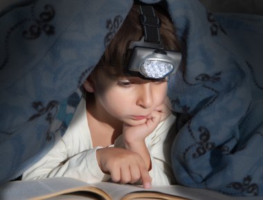 Boy reading a book under the covers with a flashlight clipart