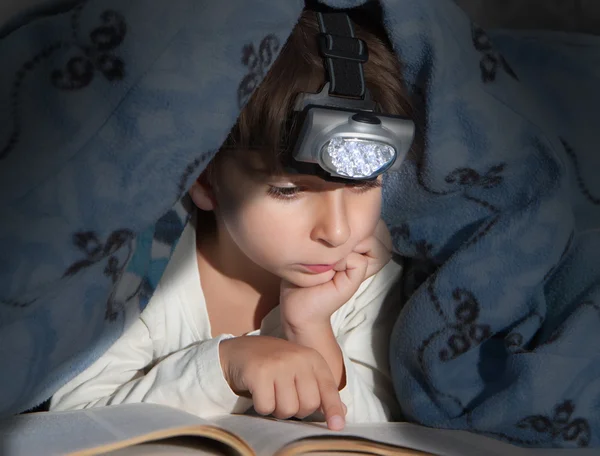 读一本书用手电筒盖下的男孩 — 图库照片