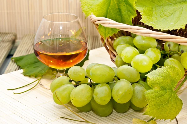 Weiße Trauben in einem Korb und ein Glas Wein — Stockfoto