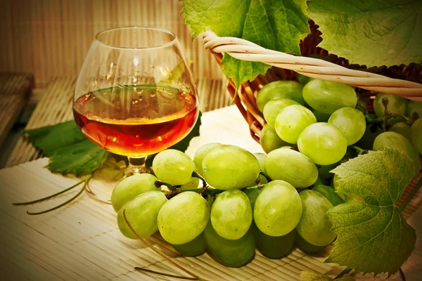 Um bando de uvas brancas numa cesta e um copo de vinho — Fotografia de Stock