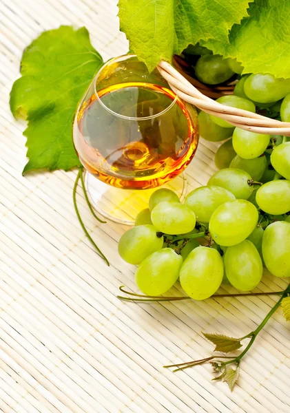 Ramo de uvas blancas en una cesta y una copa de vino —  Fotos de Stock