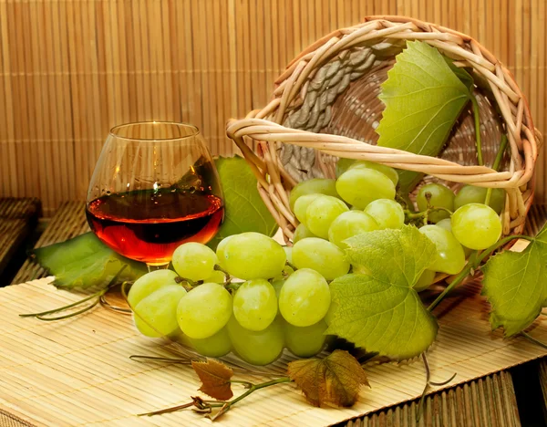 Ramo de uvas blancas en una cesta y una copa de vino —  Fotos de Stock