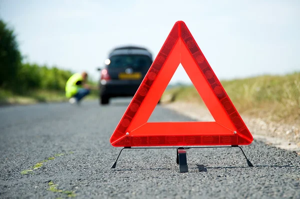 Kırmızı uyarı üçgeni ve bozuk bir araba. — Stok fotoğraf