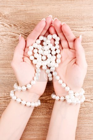 Main de femme avec des perles sur fond en bois 